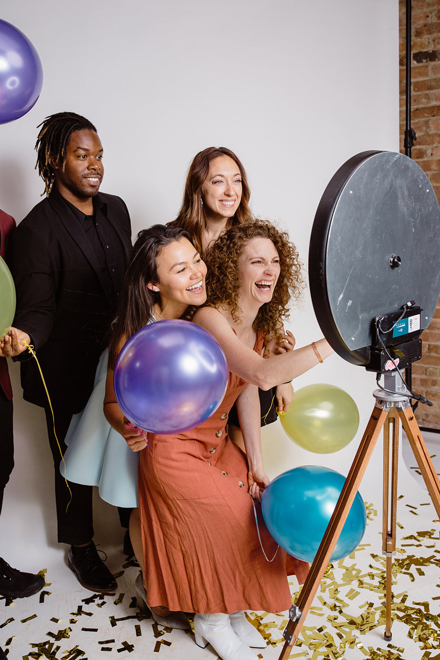 four people are delightedly using the Gifyyy Photo Booth. They have balloons.