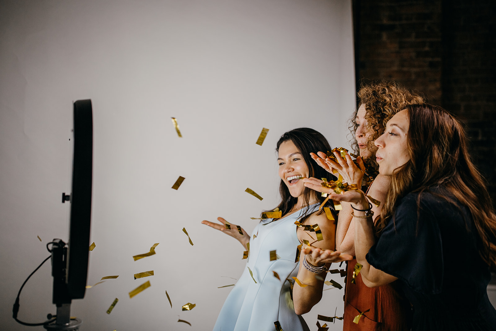 three people are blowing gold confetting towards the photo booth